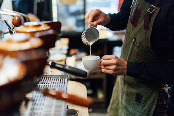 A barista pouring cream into a coffee cup