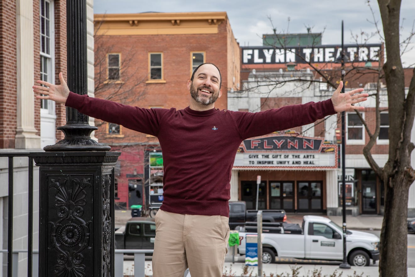 A man stands with his arms spread wide in front of the Flynn Theatre in Burlington Vermonrt