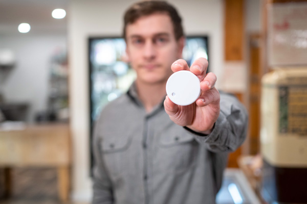 Jesse Thornburg of Grid Fruit holds a sensor beacon at Mach’s Market in Pawlet. The sensor beacon measures certain characteristics of the environment where they're placed—such as a refrigerator or freezer—and send those measurements to a nearby microcomputer.