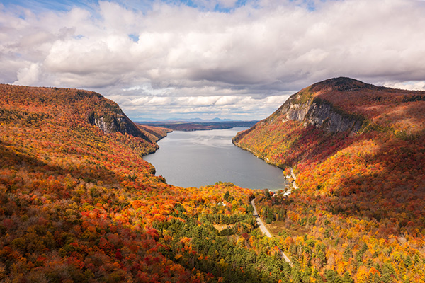 A lake seen from above in fall with brightly colored trees covering two mountains framing the water. 