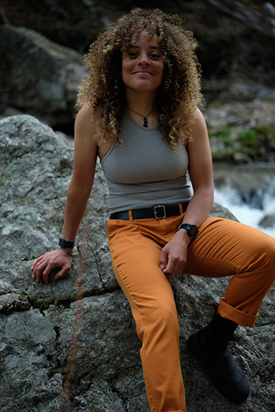 A person sitting on a rock smiles at the camera in this portrait-style image.