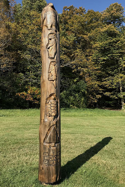 A historic Abenaki totem outside in the summer with intricate carvings in wood.