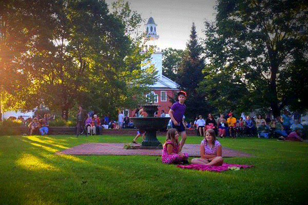  People gather on the grass outside in the summer at a festival on a sunny day. 