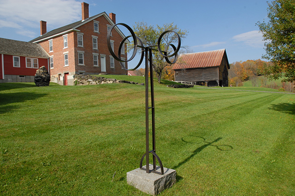  A brown wooden building seen from outside in the summer with sculptures around. 